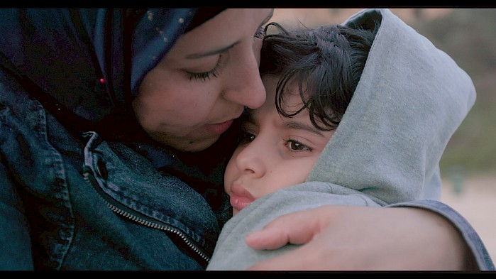 Zahra holds her youngest son on the beach. She tells him that she hid him inside her heart while they crossed the Aegean Sea.